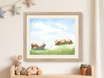 A framed watercolor art print depicting a pastoral landscape with sheep on a green hill under a blue sky, styled on a cream wall above a wooden shelf with a plush bunny, wooden toy car, and small potted succulent.