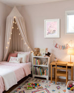 A styled children's bedroom featuring a canopy bed with blush pink bedding and star string lights, a white bookshelf with toys and books, a wooden desk with a chair and lamp, and a colorful rug on the floor.