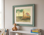A framed watercolor art print of a camel in a desert landscape, hung on a light-colored wall above a white shelf with a stuffed giraffe and books.