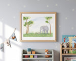 A framed watercolor painting of an elephant in a grassy field under trees, displayed on a light gray wall in a children's room setting with a wooden shelf, toys, and books.