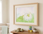 Framed sea turtle watercolor art print hanging on a neutral wall in a cozy nursery above a shelf with wooden toys.
