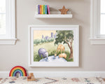 A framed watercolor art print depicting safari animals (elephant, giraffe, and zebra) in a grassy landscape, styled on a beige wall in a children's room setting with a shelf, books, and a rainbow toy below.