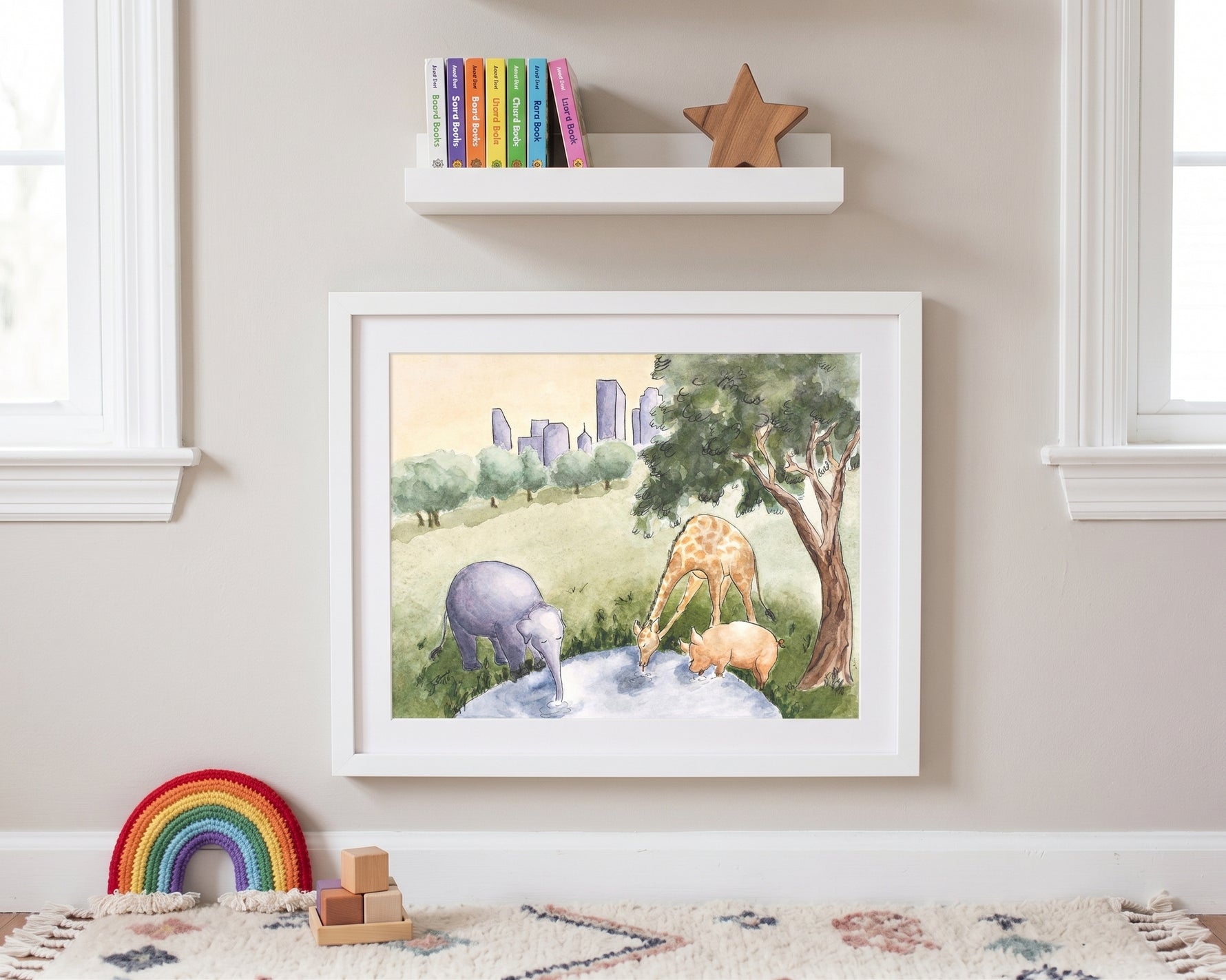 A framed watercolor art print depicting safari animals (elephant, giraffe, and zebra) in a grassy landscape, styled on a beige wall in a children's room setting with a shelf, books, and a rainbow toy below.